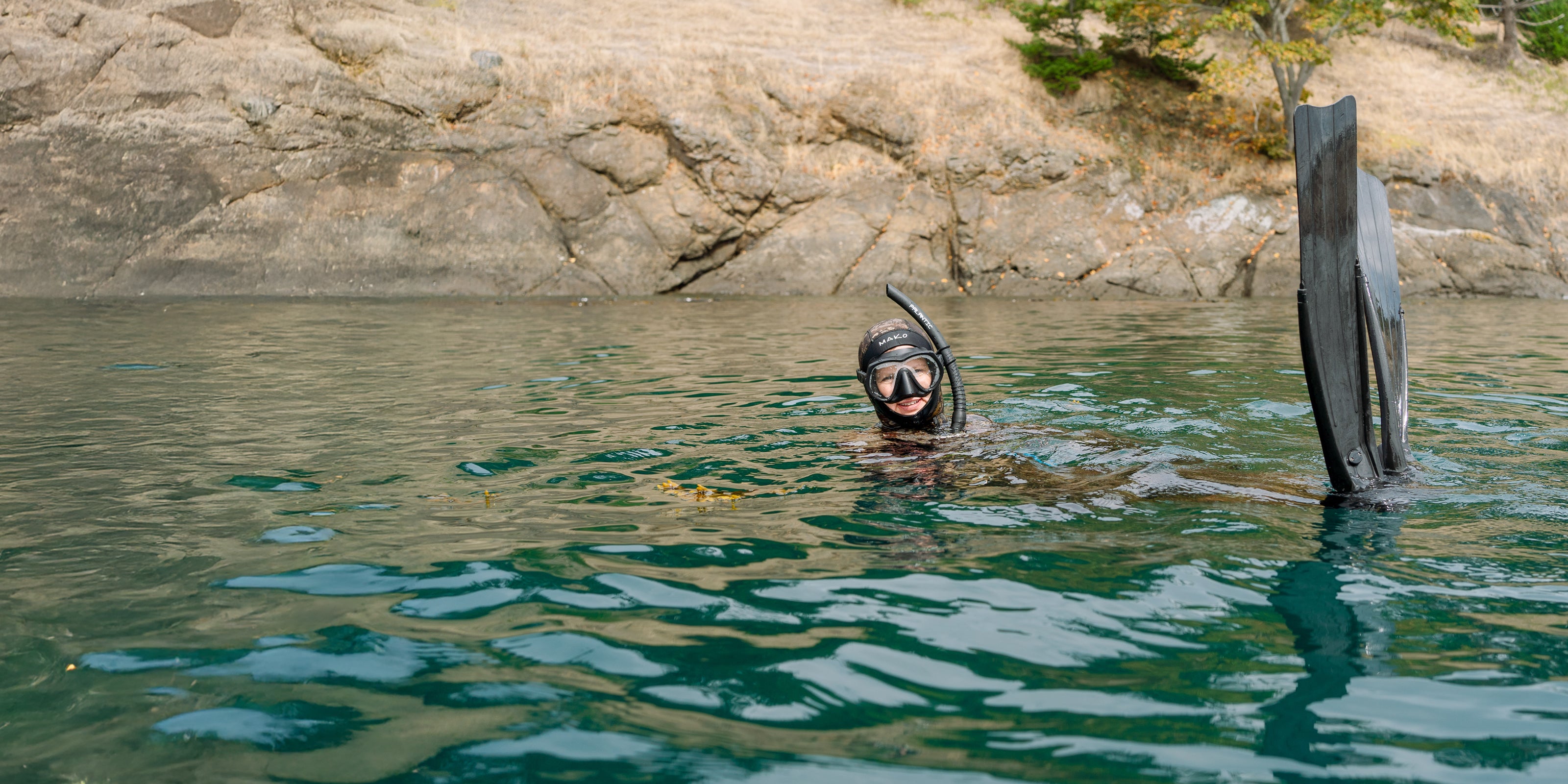 Person snorkeling in a body of water with rocky cliffs in the background