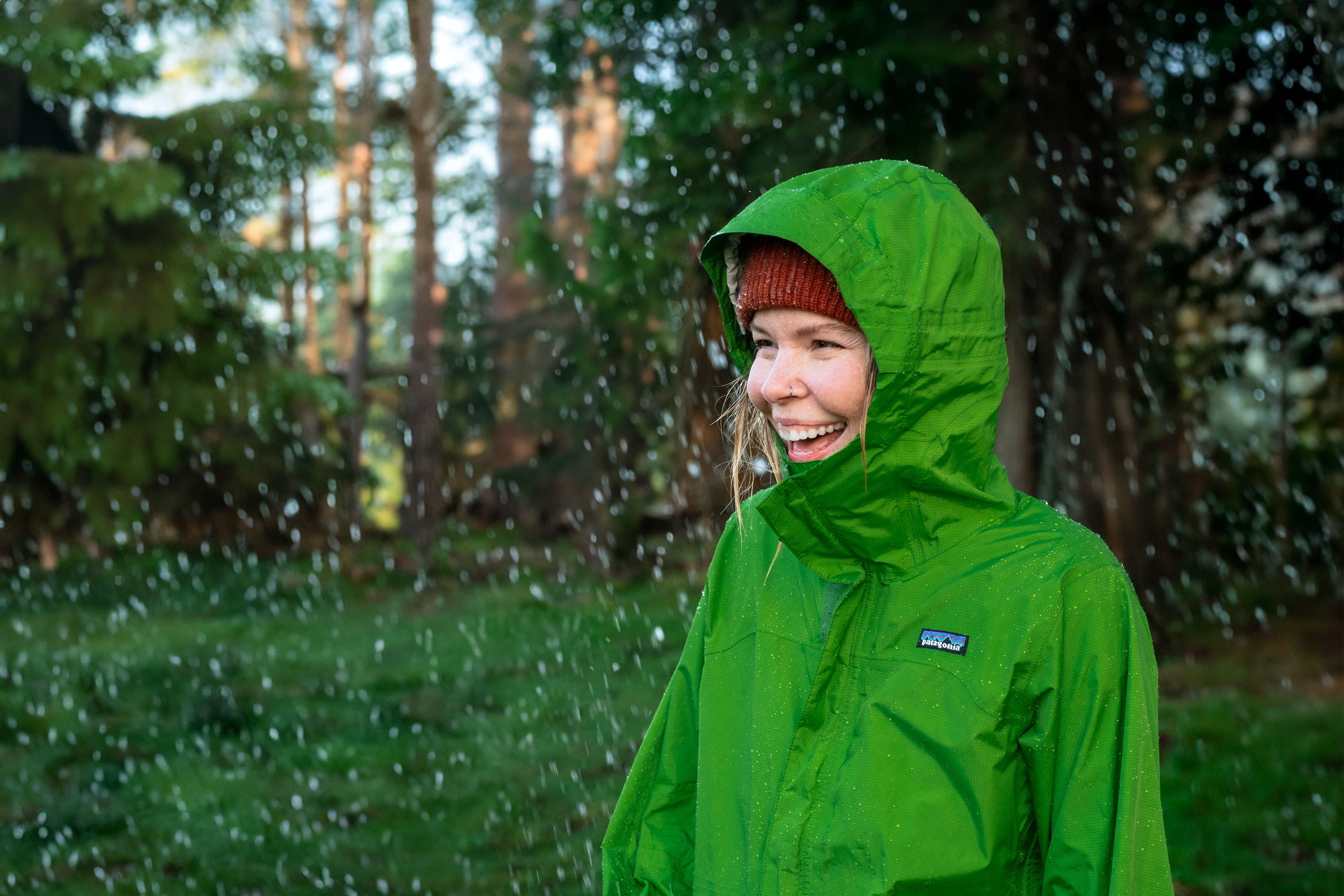 Person wearing a green raincoat with a visible brand logo, standing outdoors in light snowfall.