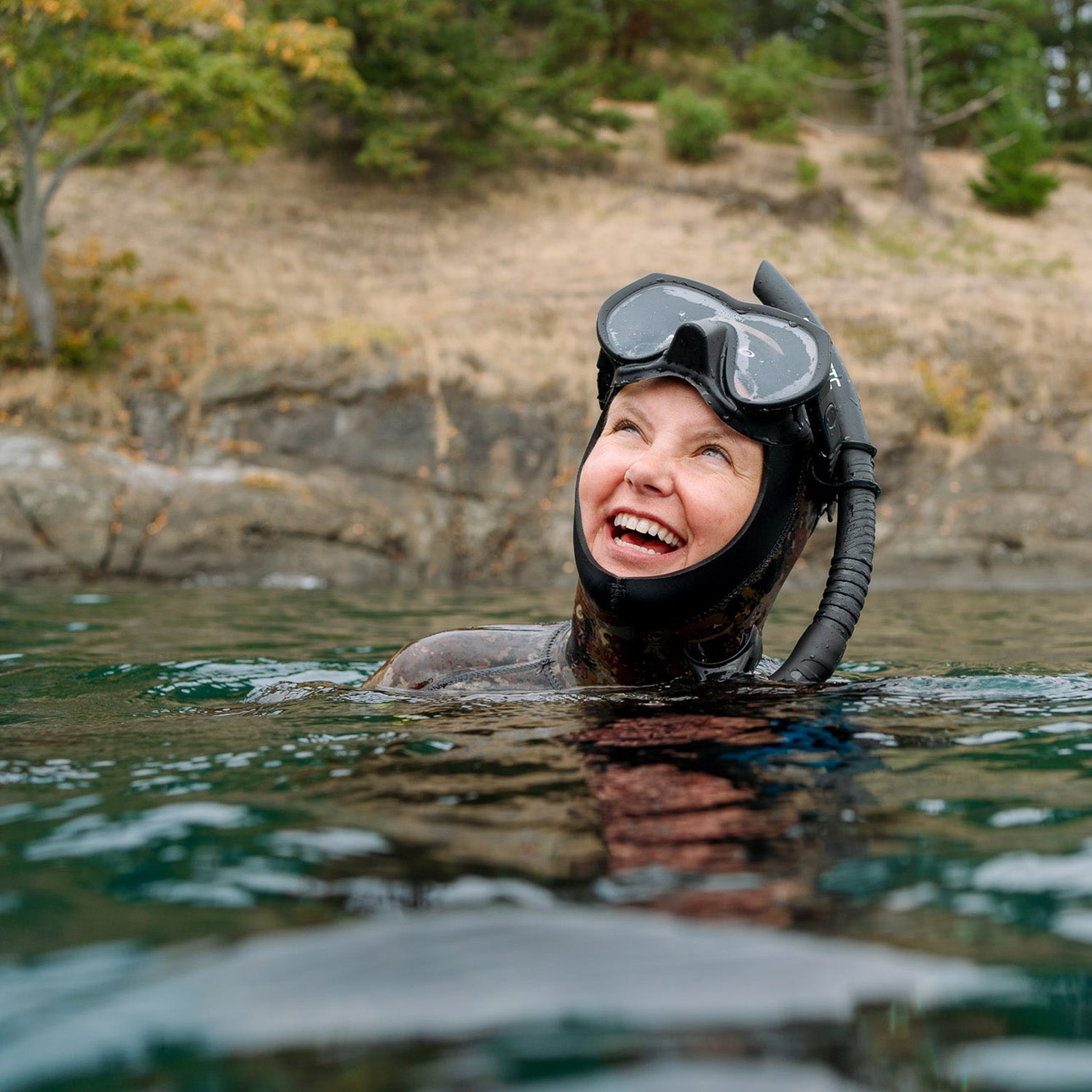 Person wearing scuba diving gear in a natural setting with trees and rocks.