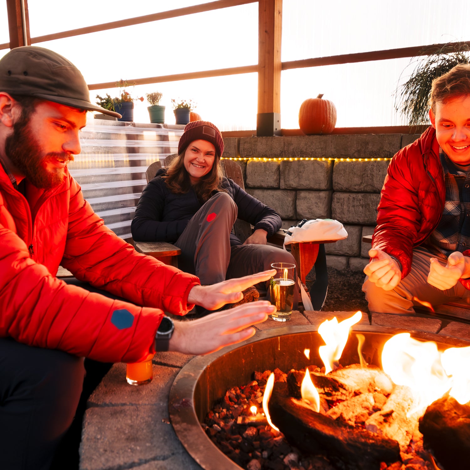 Three people sitting around a fire pit on a patio, enjoying drinks and each other's company.