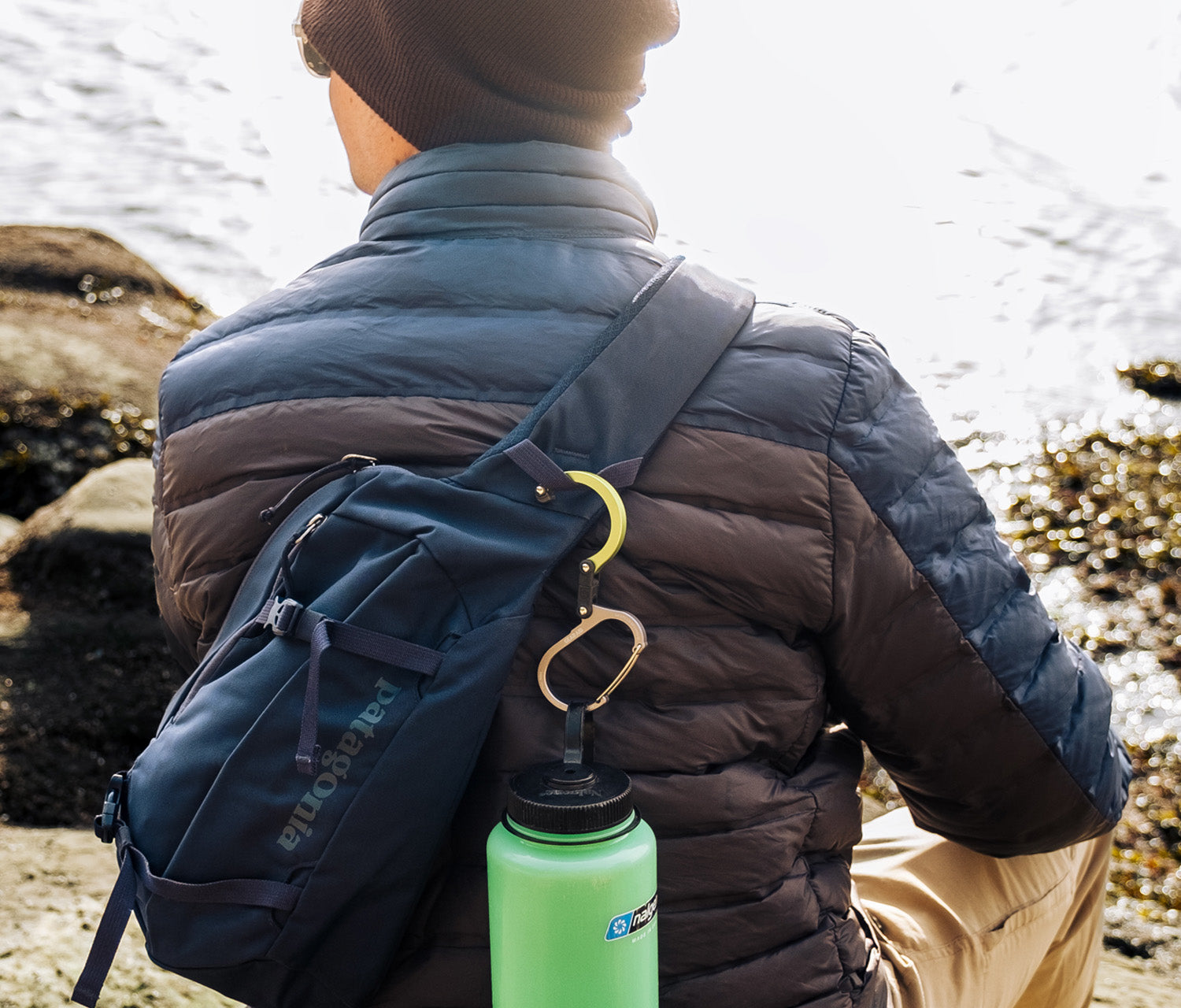 Person wearing a blue backpack with a green water bottle, standing by a body of water.