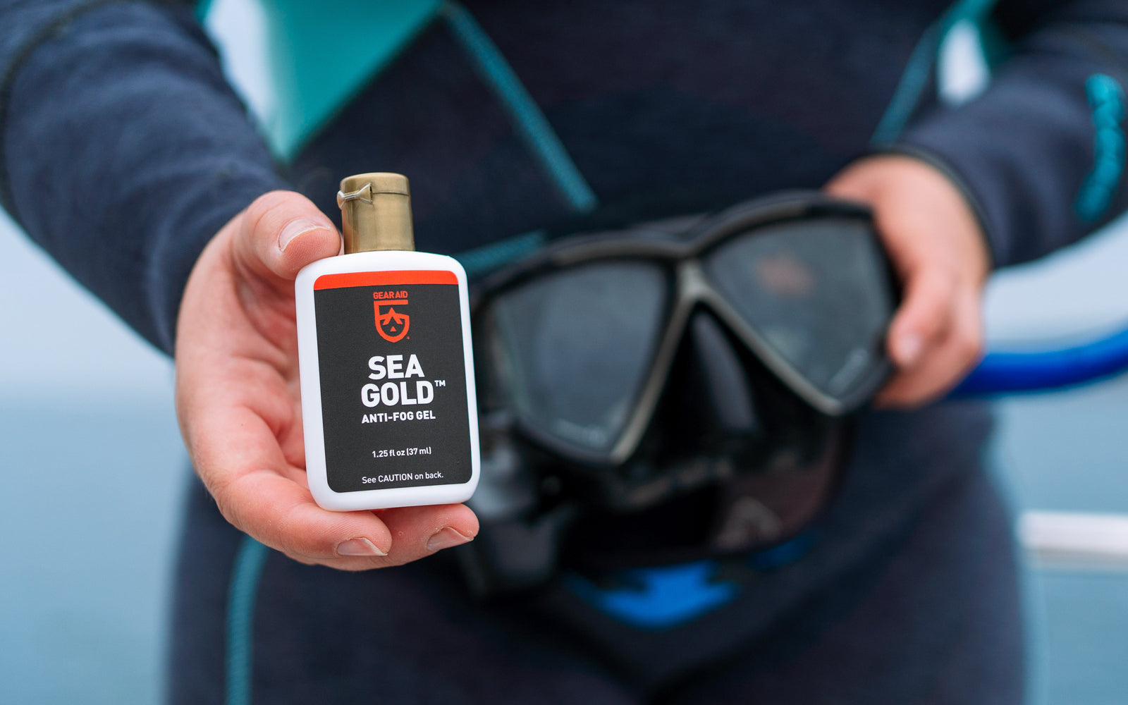 Person holding a bottle of Sea Gold Anti-Fog solution with diving goggles in the background