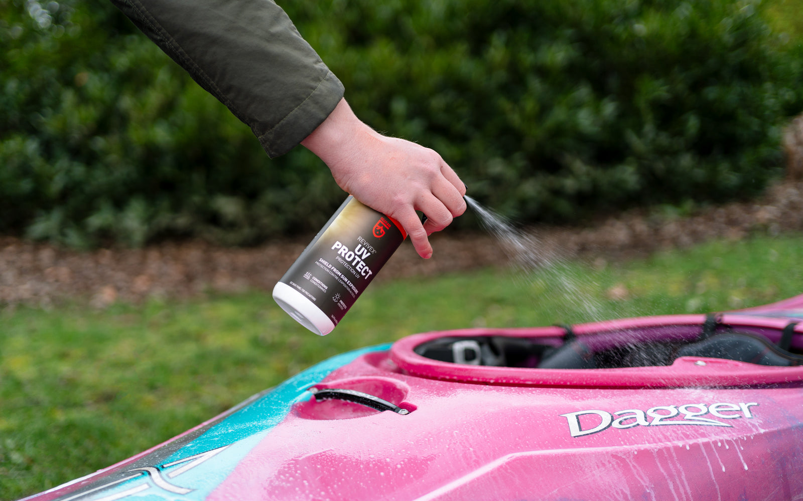 Person using a spray bottle of UV Protect on a pink and blue kayak with 'Dagger' branding.