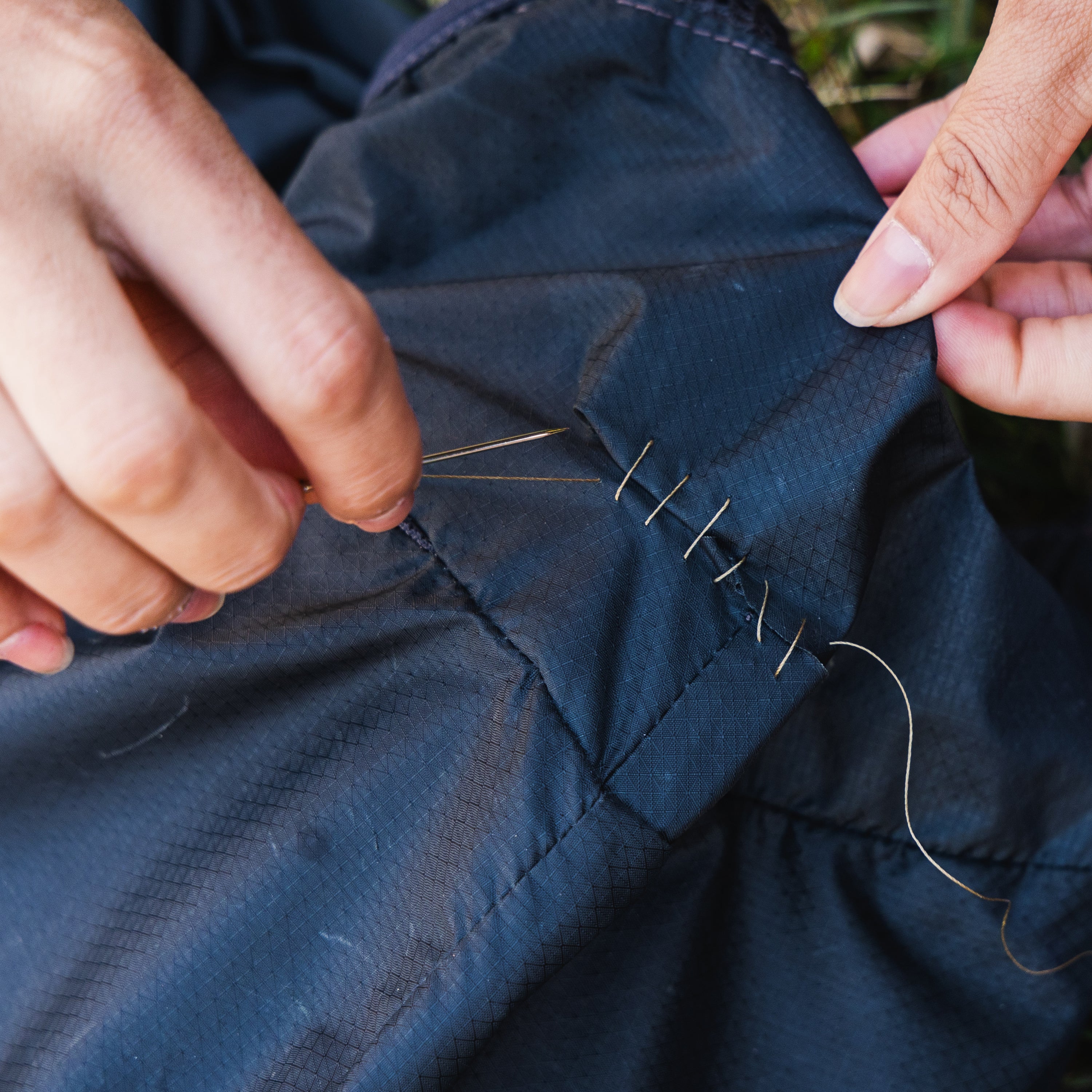Person sewing blue fabric with a needle and thread