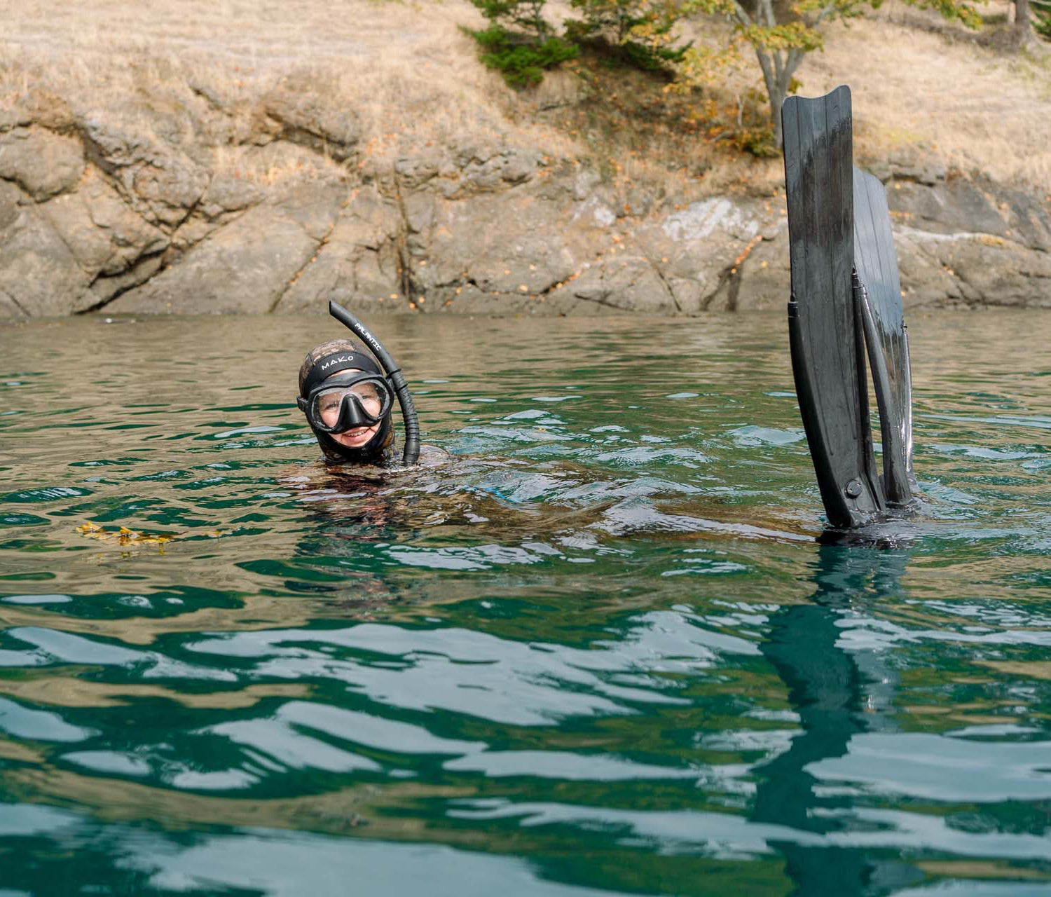 Person snorkeling with a fins attached to their back in a body of water.