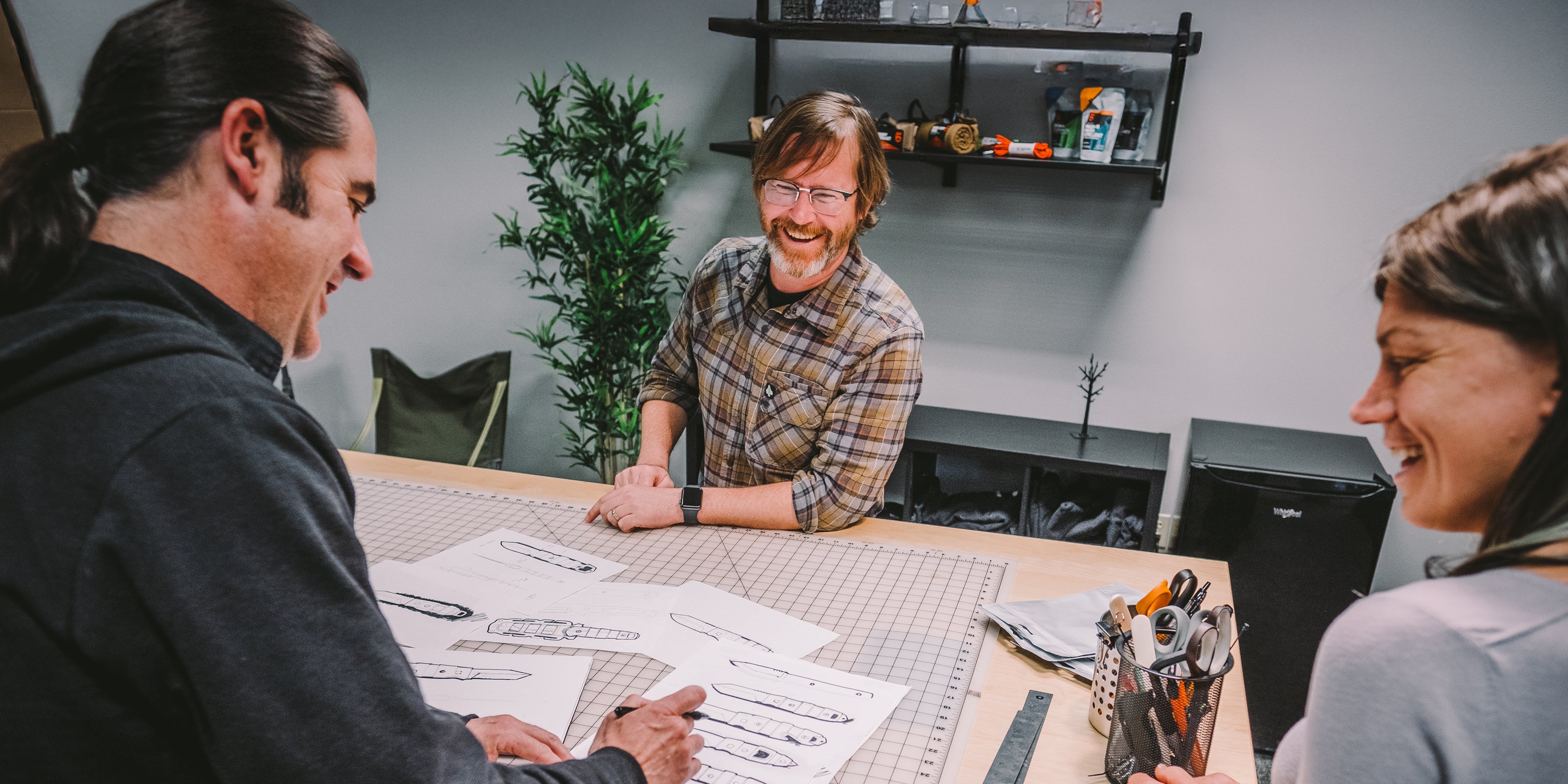 Three people sitting around a table with papers, smiling and engaged in a discussion.