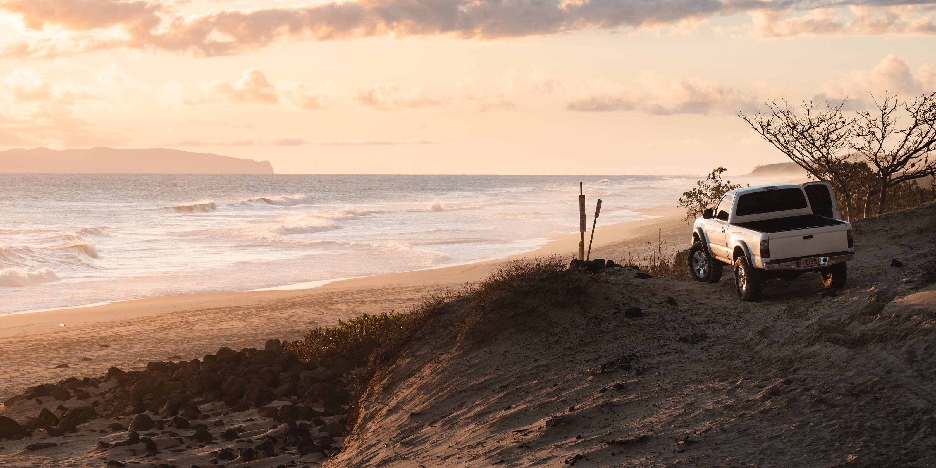 White truck parked on a sandy beach with ocean and sunset in the background
