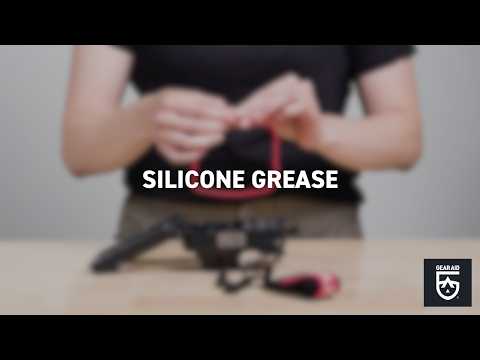 Blurred video cover showing a person stretching a red rubber seal above scuba-diving equipment on a tabletop, with the title “SILICONE GREASE” centered and the Gear Aid logo in the bottom-right corner.