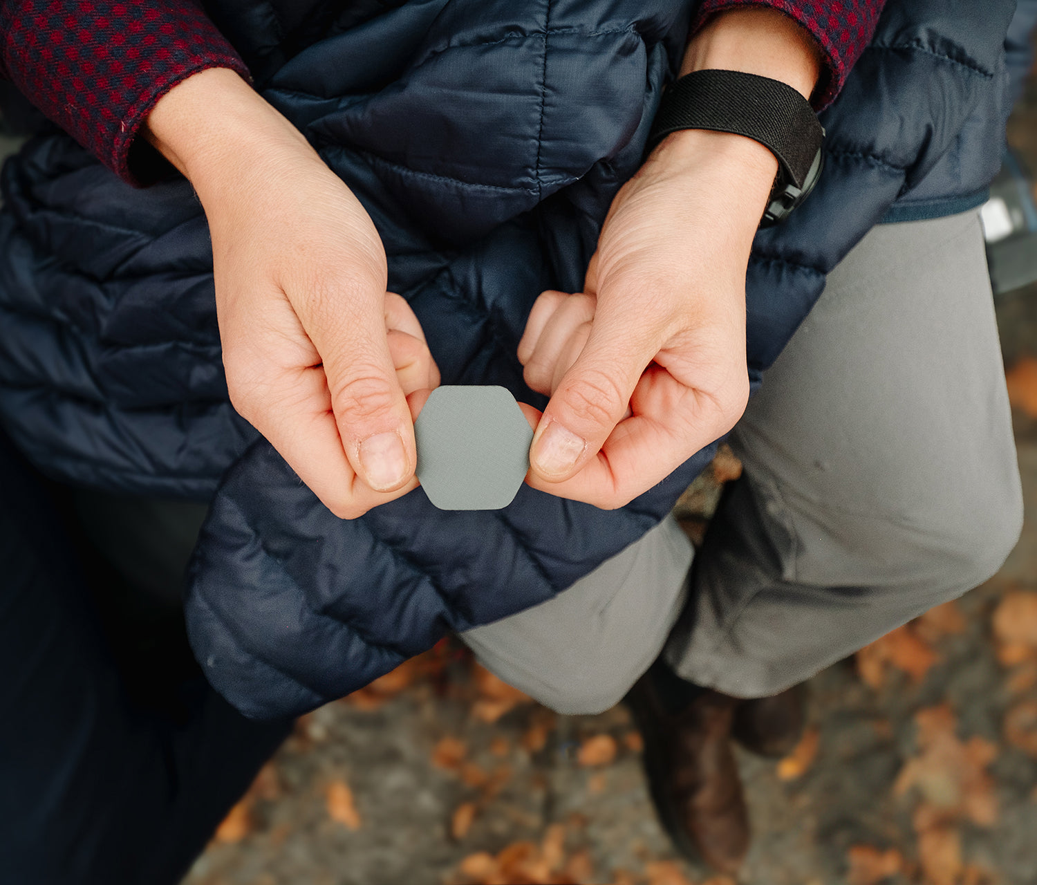 Person wearing a navy puffer jacket holding a small gray hexagonal object outdoors.
