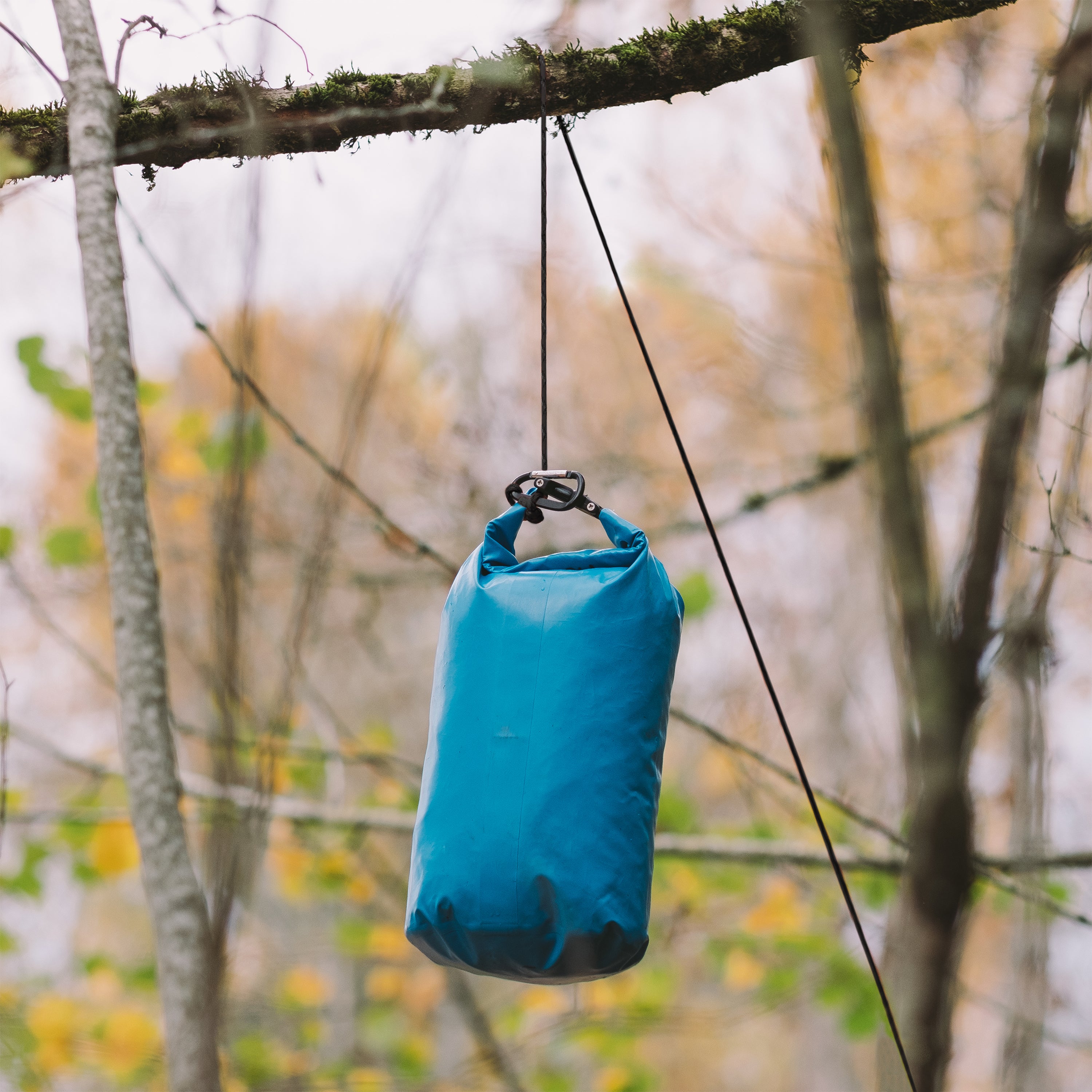 GearAid paracord attached to a blue dry bag and hung over a branch in the woods