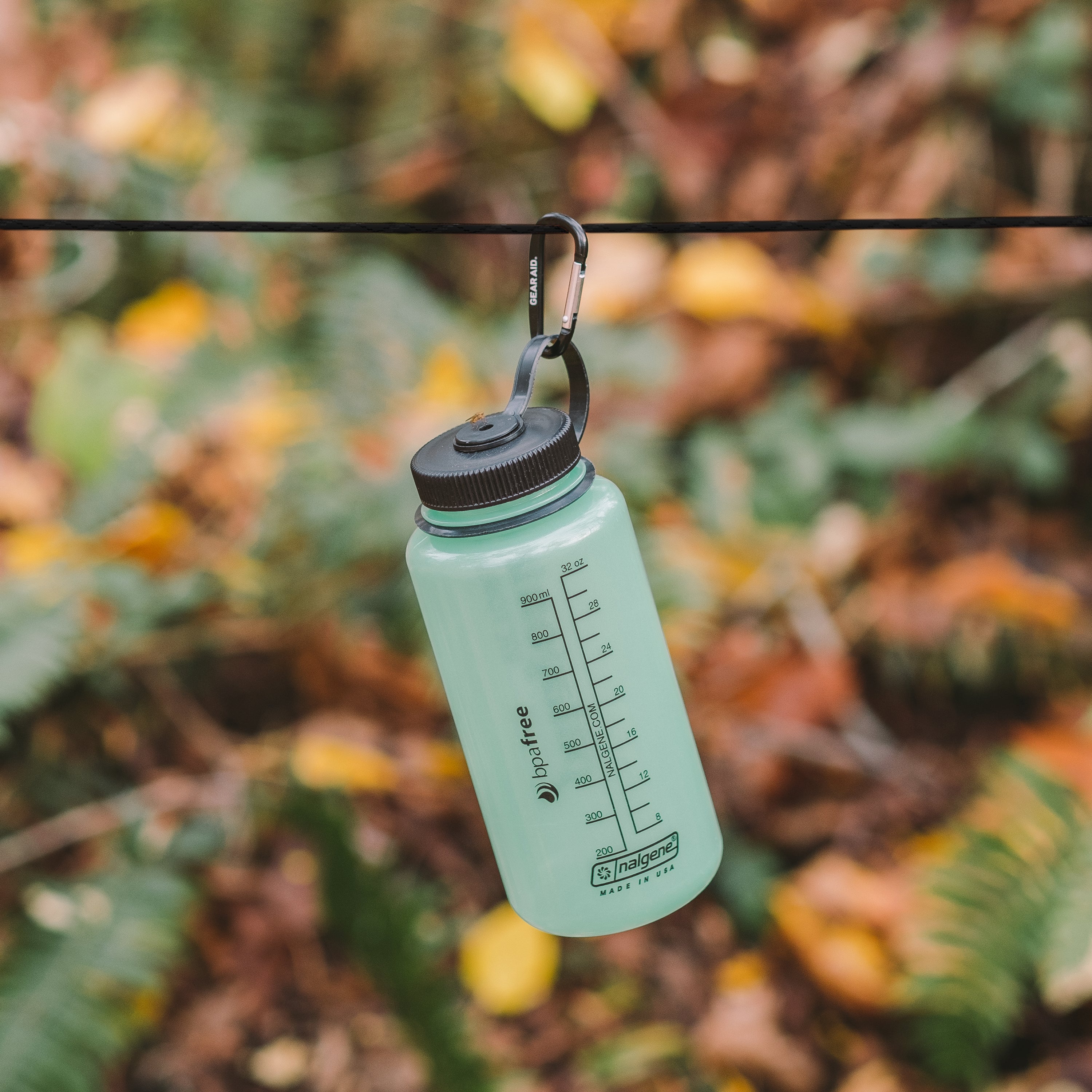 Transparent green Nalgene clipped with a small black carabiner to a piece of paracord, foliage in the background
