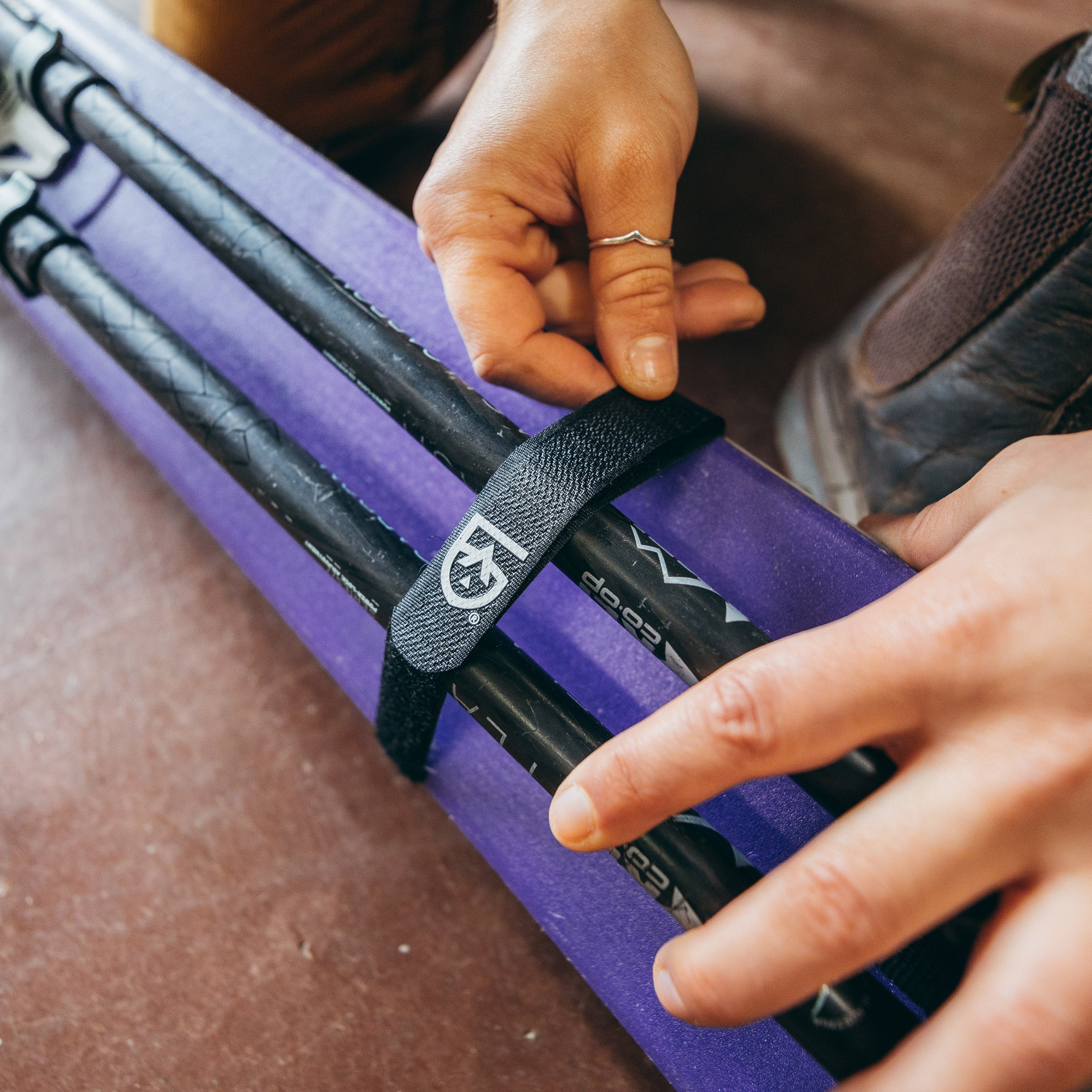 Hands placing a Fast Wrap with Utility Strap 3-4 Inches around a pair of ski poles and skis
