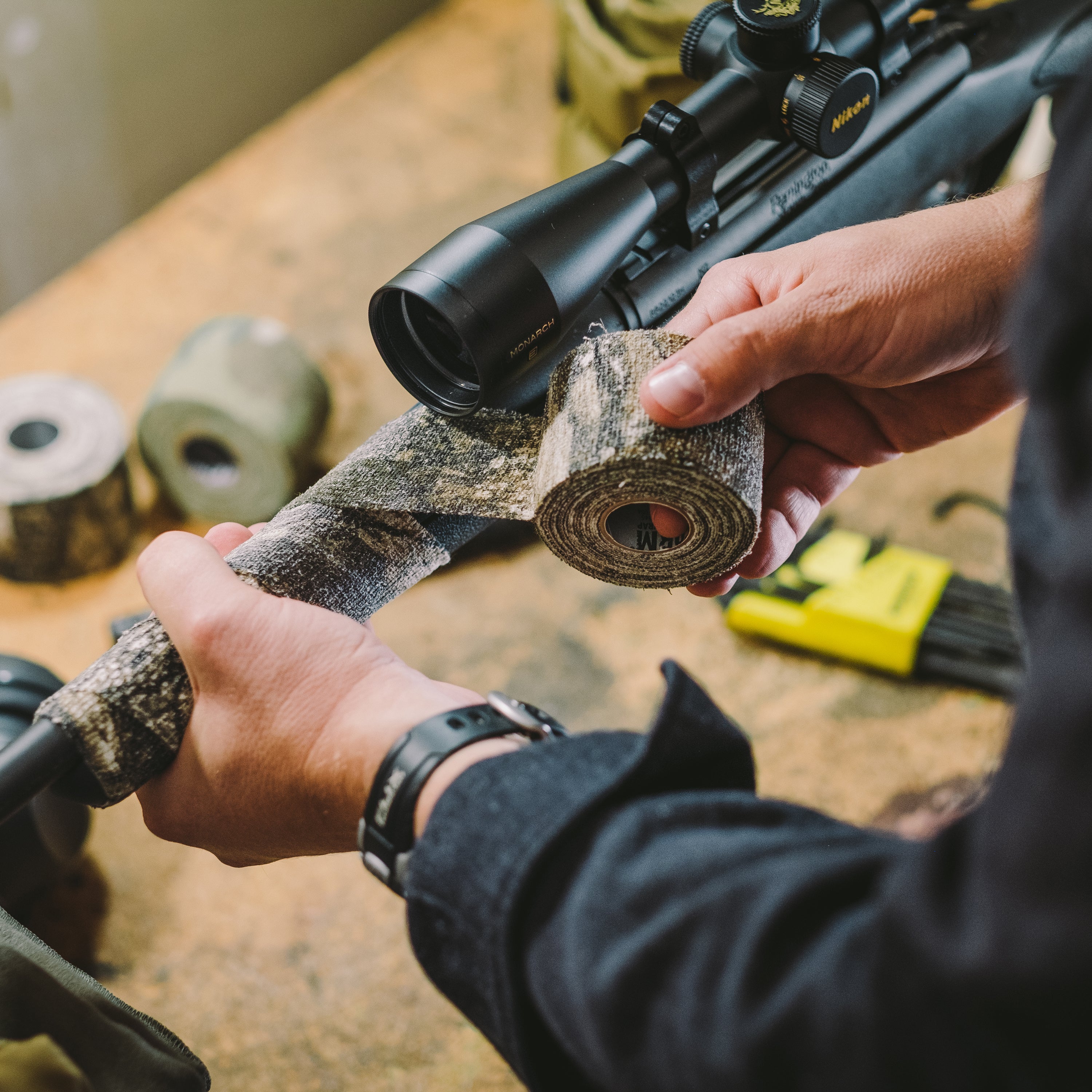 Hands unrolling Camo Form and wrapping it around hunting gear above a workbench
