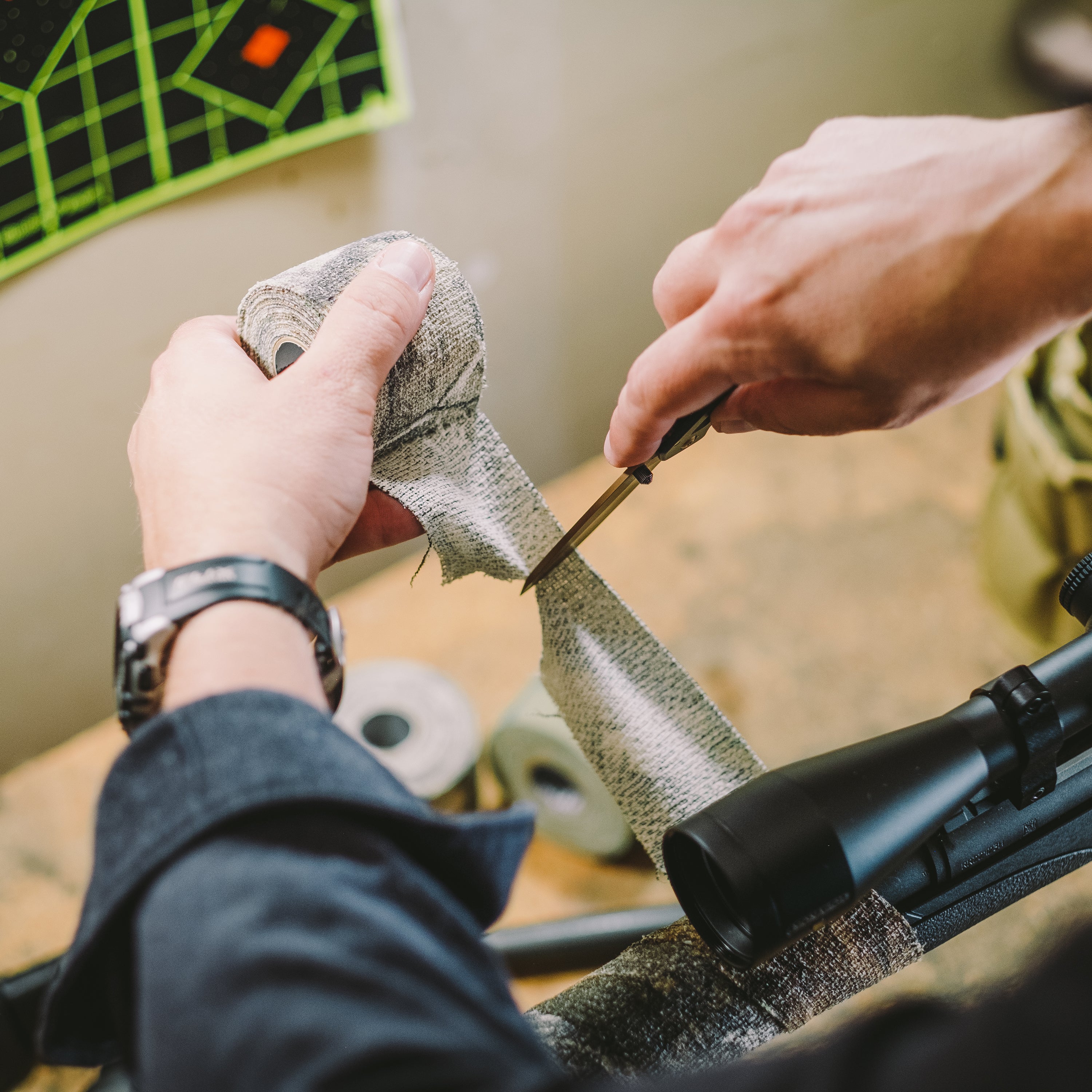 Person using a blade to cut a piece of Camo Form that they are using to wrap hunting gear with
