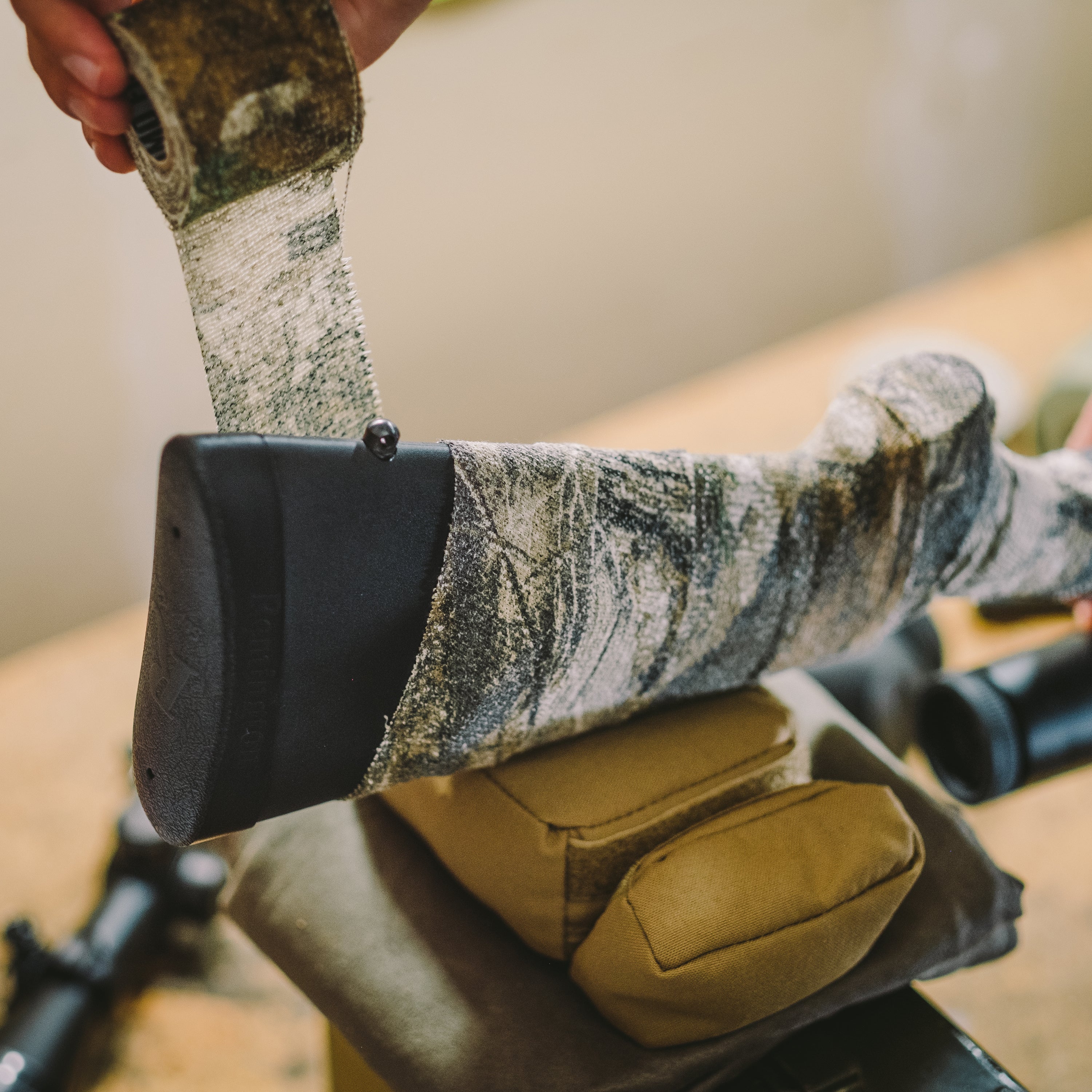 Hand unrolling Camo Form and wrapping it around hunting gear above a workbench