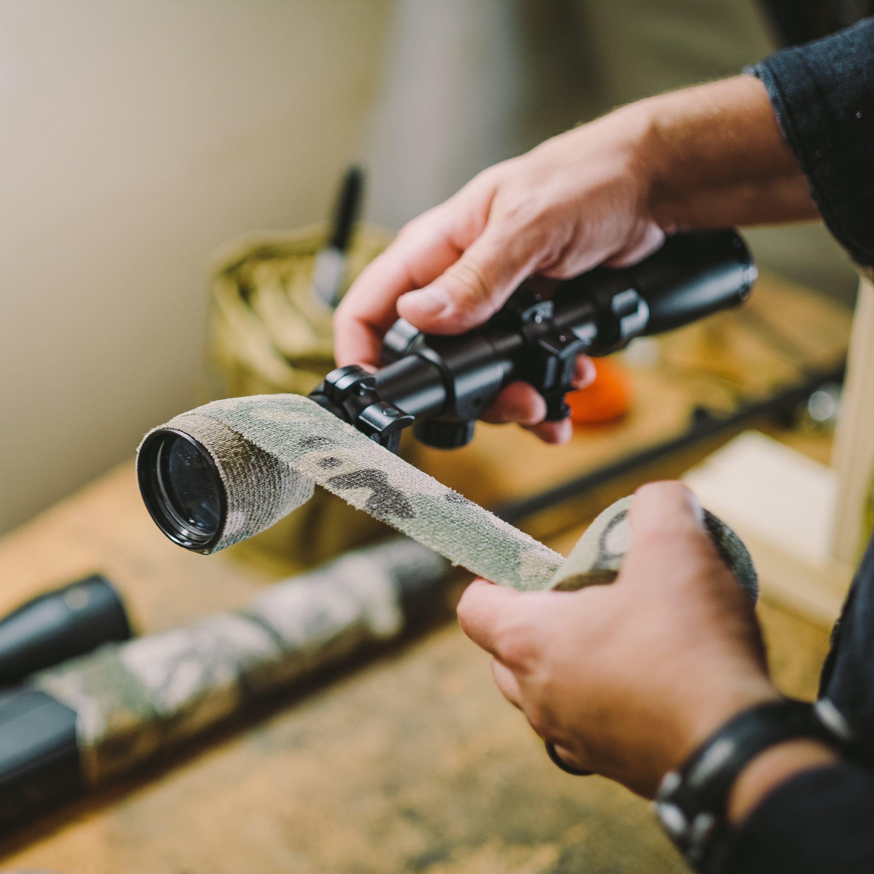 Hands unrolling Camo Form and wrapping it around a scope above a workbench