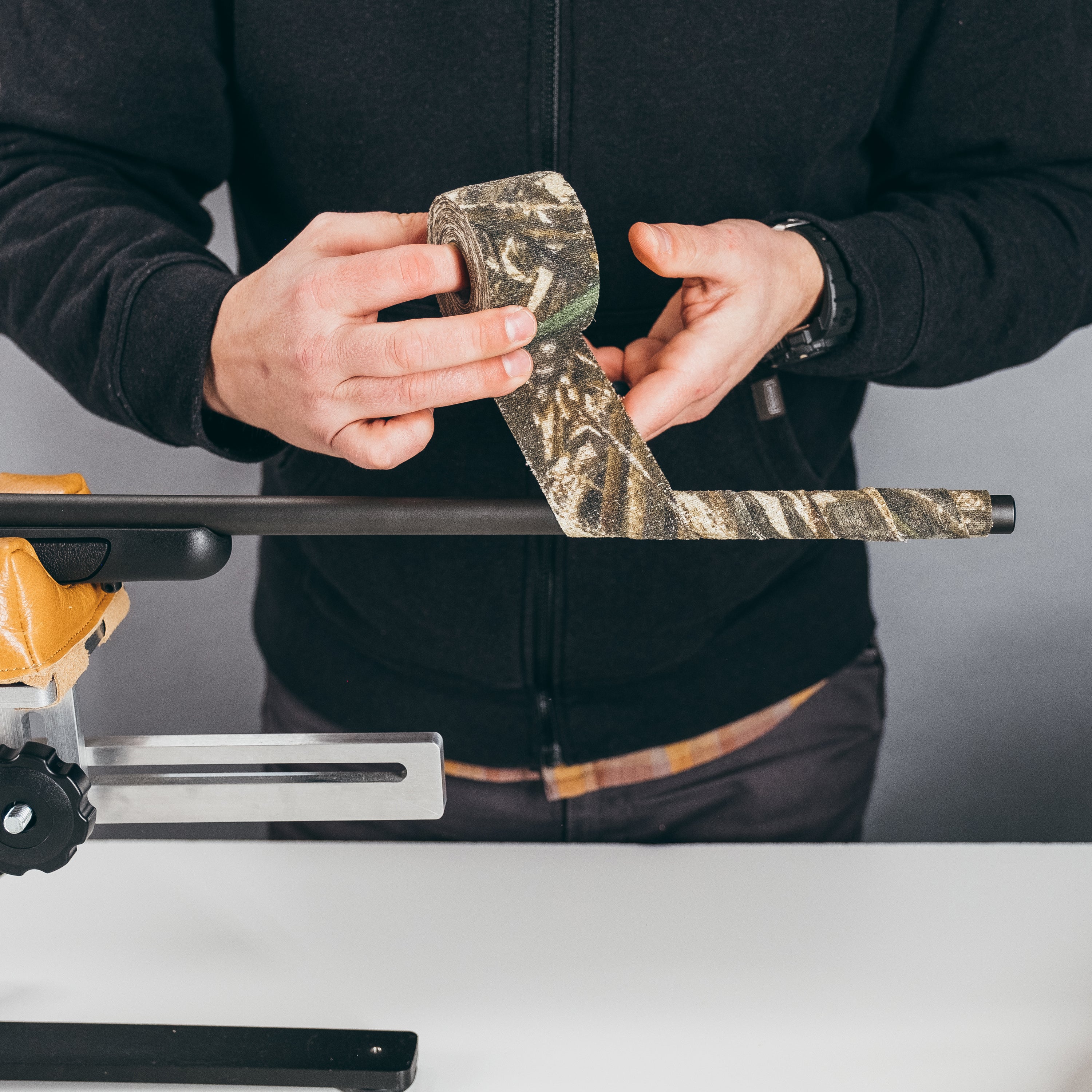 Hands unrolling Camo Form and wrapping it around hunting gear above a white workbench